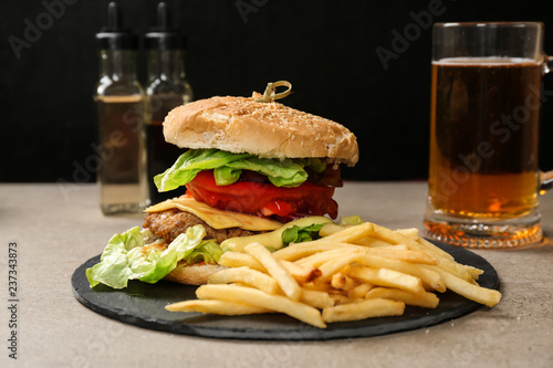 Slate plate with tasty burger and french fries on table