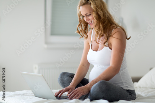 Happy pregnant woman using laptop in bedroom
