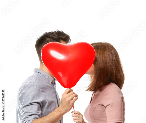 Young couple hiding behind heart-shaped balloon on white background. Celebration of Saint Valentine's Day