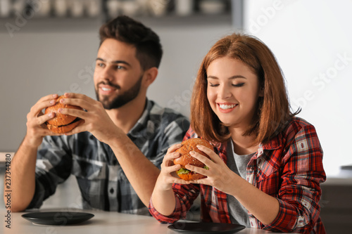 Young couple eating tasty burgers at home