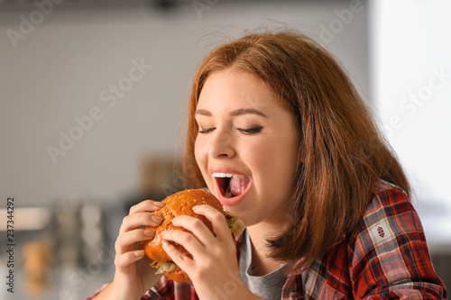 Young woman eating tasty burger at home