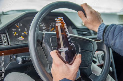 A drunken man driving a car with a bottle of alcohol in his hand.A man holds a driving wheel and a bottle of beer. © yaroslav1986