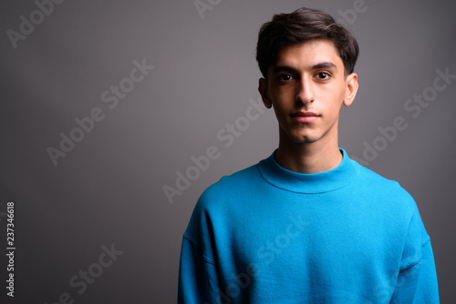 Young handsome Persian teenage boy against gray background