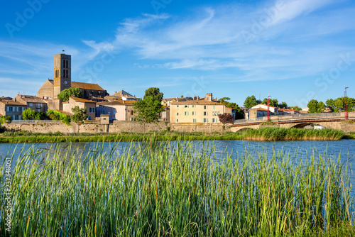 France, Trebes, near Carcassonne: Panorama skyline view of French small town with Aude river, Church Saint Etienne, green reed, cityscape, bridge and blue sky in the background - concept travel