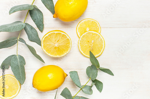 Whole and sliced fresh lemon, eucalyptus leaves on white wooden background. Flat lay, top view, copy space. Minimal fruit concept design. Yellow citrus, lemons