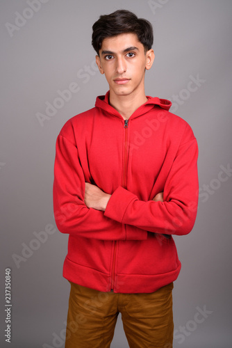 Young handsome Persian teenage boy against gray background