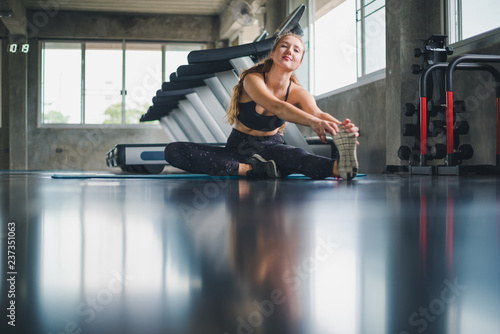 Beautiful athlete put on a sports suit. Stretching a muscle on a yoga mat. Before playing sports in the gym. She is relaxing