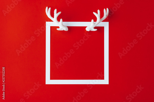 Fototapeta Poroże renifera z białą ramką na czerwonym tle. Boże Narodzenie minimalna ilość miejsca na kopię. Kartka z życzeniami.