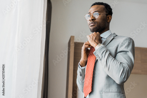 handsome african american businessman adjusting red tie in hotel room