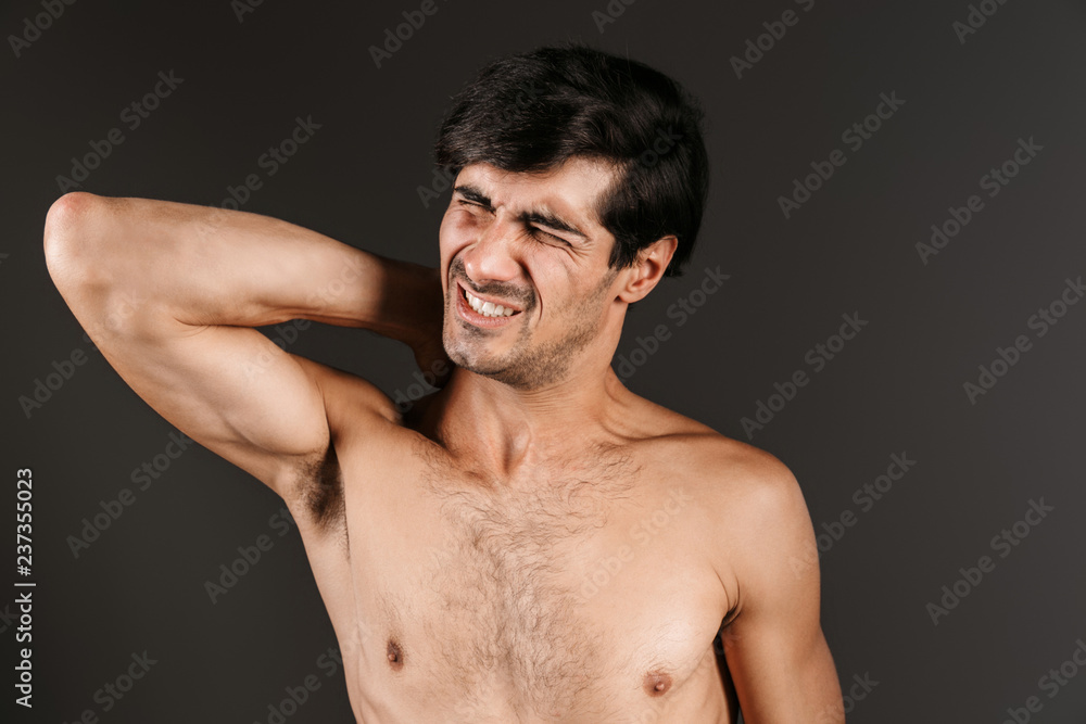 Handsome displeased young man with neck pain posing isolated over dark wall background. Handsome displeased young man with neck pain posing isolated over dark wall background.