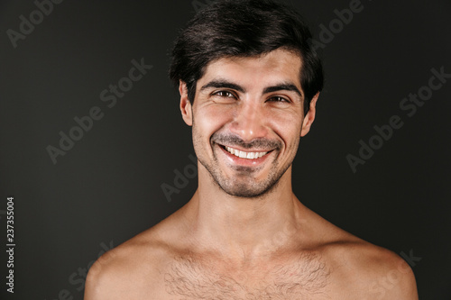 Naked young smiling man posing isolated over dark wall background.