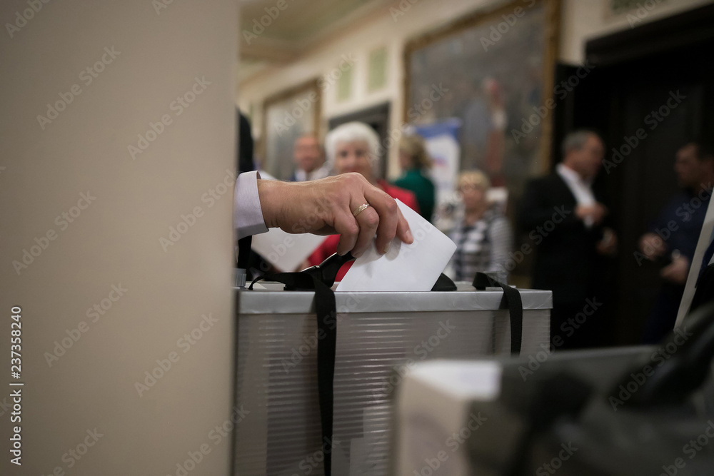 Naklejka premium Hand of a person casting a vote into the ballot box during elections