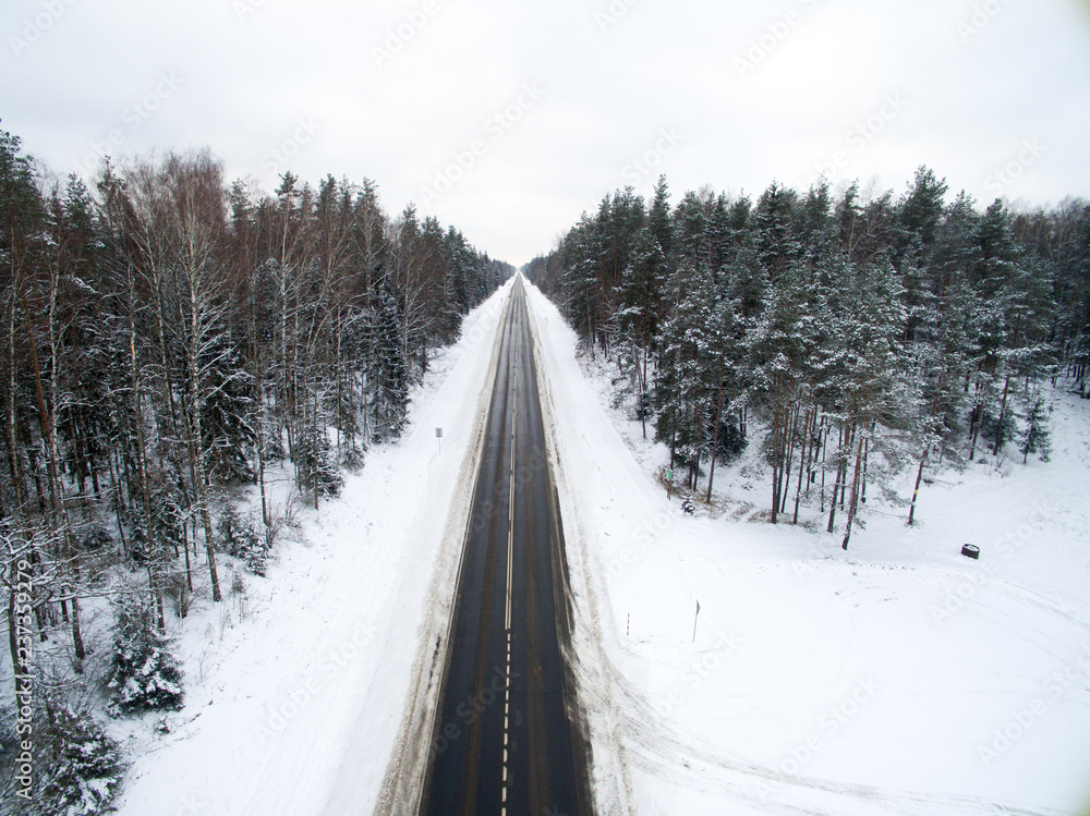 Winter forest and asphalt road. View from above. The photo was taken with a drone. Pine and spruce forest with a black road in the snow Winter forest and asphalt road. View from above. The photo was taken with a drone. Pine and spruce forest with a black road in the snow