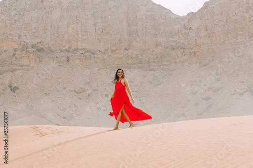 Young beautiful indian woman walking in red dress in the desert with mountains photo