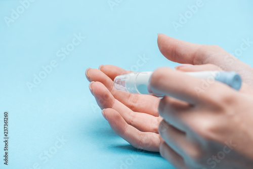 cropped view of female hands testing glucose level with needle on blue background