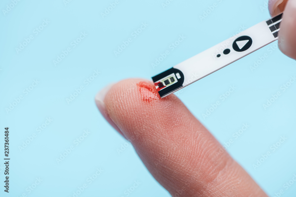 Obraz premium close up of fingers and diabetes test strip isolated on blue background