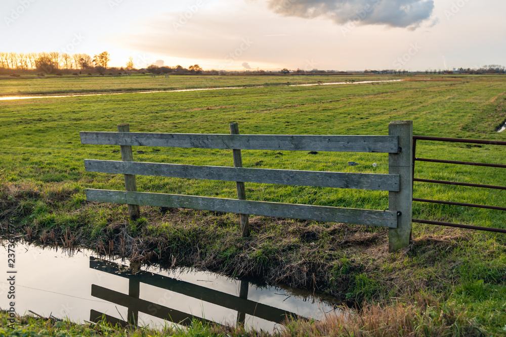 Fototapeta premium Wooden fence reflects in the mirror-smooth water surface of a polder ditch