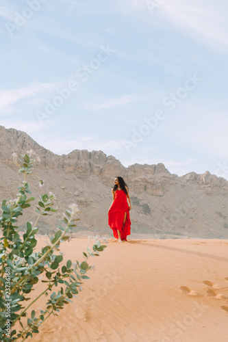 Young beautiful indian woman in red dress standing in the desert with her hands above the head