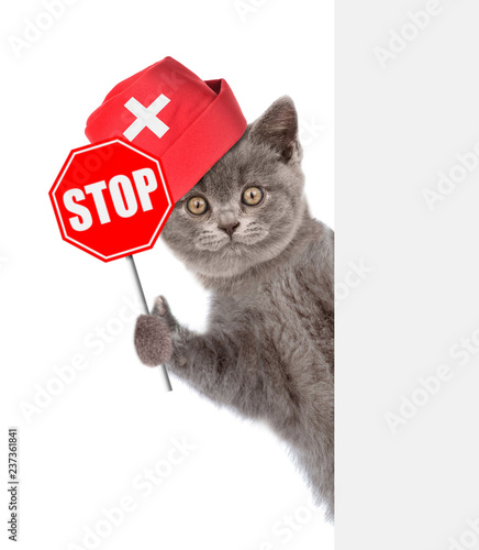Funny kitten in medical hat with sign stop in paw behind empty white banner. isolated on white background