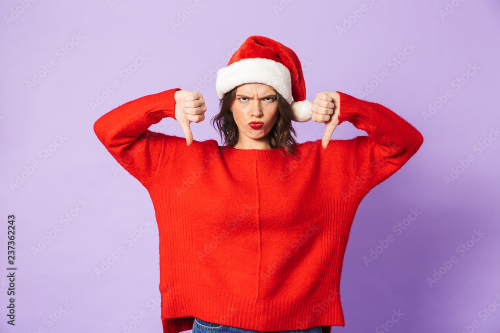 Displeased young woman wearing christmas hat isolated over purple background showing thumbs down gesture.
