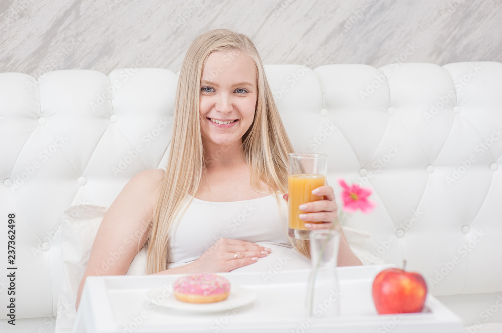 Smiling pregnant woman with juice and donut on the bed Smiling pregnant woman with juice and donut on the bed