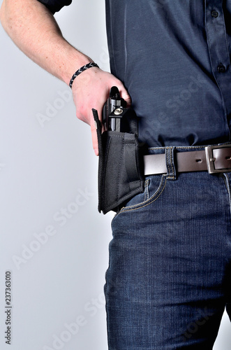 Man pulling out a pistol gun from the holster on belt, blue jeans, black shirt