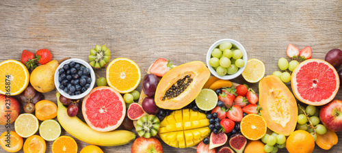 Top view of rainbow colored fruits  strawberries blueberries  mango orange  grapefruit  banana papaya apple  grapes  kiwis on the grey wood background  copy space for text  selective focus