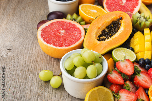 Variety of fruits  strawberries blueberries  mango orange  grapefruit  banana papaya apple  grapes  kiwis on the grey wood background  copy space for text  selective focus