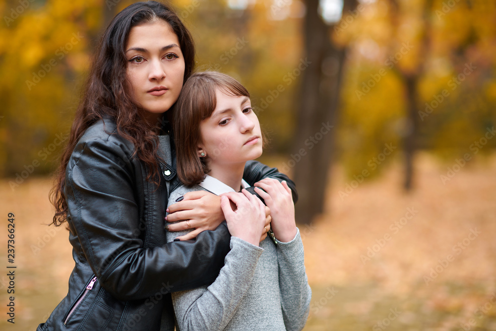Fototapeta premium Pretty woman and teen girl are posing in autumn park. Beautiful landscape at fall season.