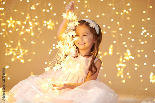 girl child is playing with christmas lights, yellow background, pink dress