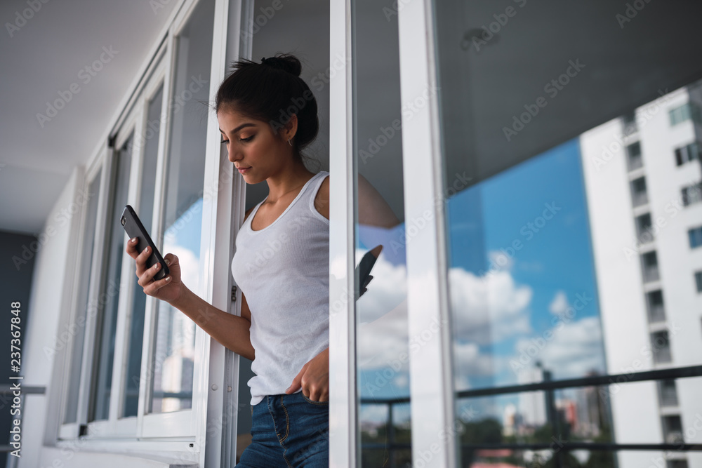 Attractive young lady using smartphone near windows of balcony Attractive young lady using smartphone near windows of balcony