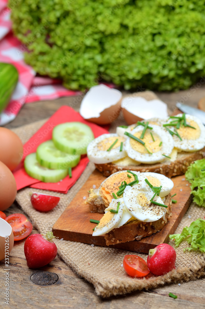 Wholegrain bread with butter, hard-boiled eggs, fresh radishes, tomatoes, salad and cucumbers in background, vertical photo Wholegrain bread with butter, hard-boiled eggs, fresh radishes, tomatoes, salad and cucumbers in background, vertical photo