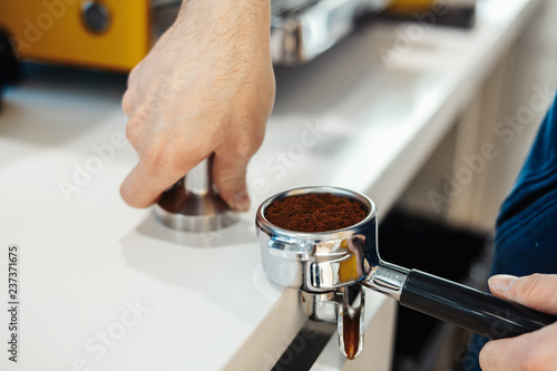 Barista hands holding portafilter and coffee tamper making an espresso coffee.