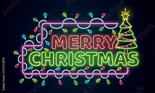 Neon text Merry Christmas decorated with lighting garland and xmas tree on brick wall background.