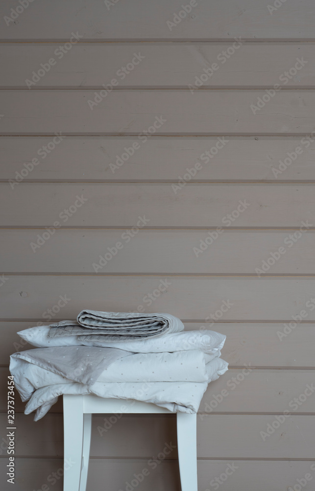 White and grey bedroom linens at white chair, wooden beige background, cozy home laundry photo White and grey bedroom linens at white chair, wooden beige background, cozy home laundry photo