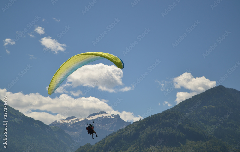Silhouette of a paraglider, mountains covered with forest, blue sky with clouds. Interlaken, Switzerland. Silhouette of a paraglider, mountains covered with forest, blue sky with clouds. Interlaken, Switzerland.