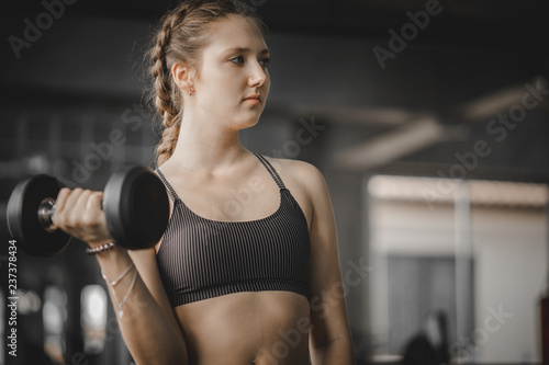 Fit beautiful young woman caucasian posing at the camera in sportswear. Young woman holding dumbbell during an exercise class in a gym. Healthy sports lifestyle, Fitness concept.