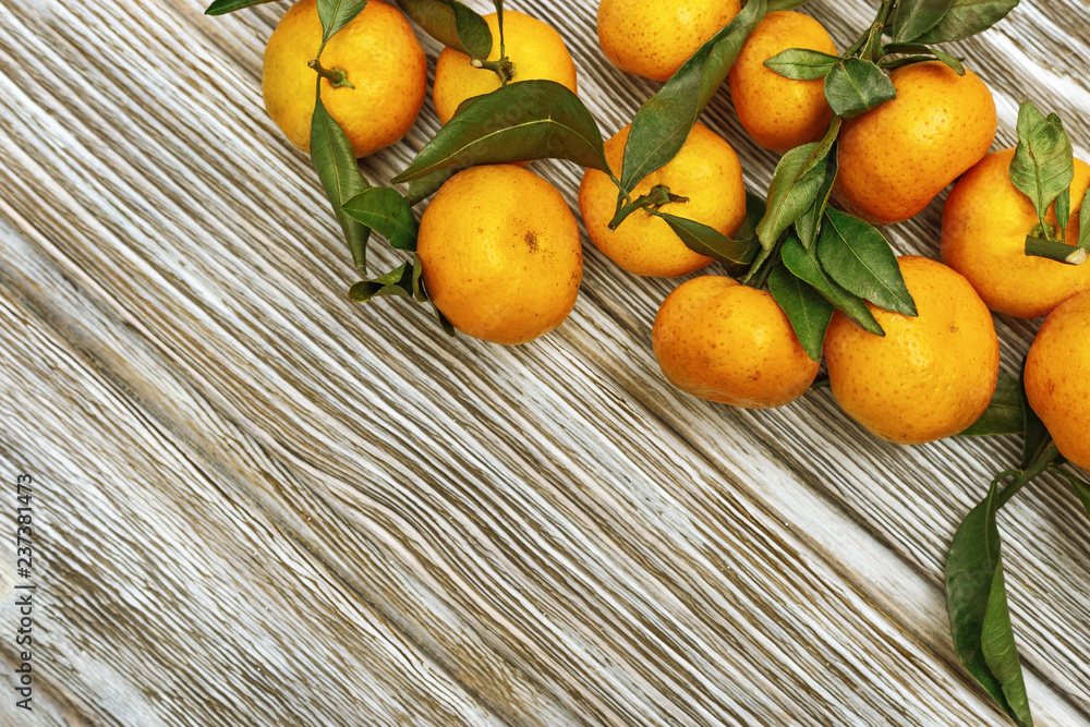 Heap of tangerines with green leaves on rustic wooden background with copy space. Fresh orange fruits.