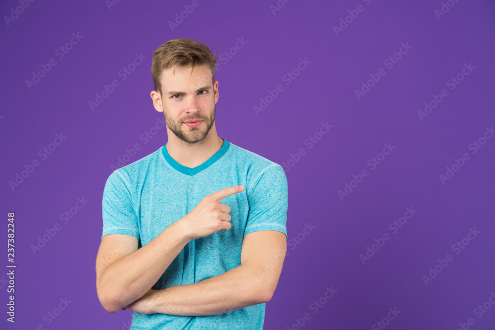 Obraz premium Look here. Man muscular handsome unshaven guy on violet background pointing finger copy space. Masculinity concept. Man with strong muscular arms. Does having muscular body make you more confident