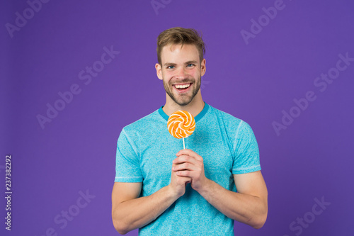 Taste of childhood. Man with bristle likes lollipop. Cheat meal concept. Sugar harmful for health. Guy hold lollipop candy violet background. Man handsome macho eat big colorful sweet lollipop