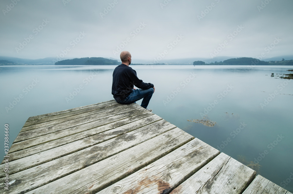 Lonely man sitting on jetty looking at distance Lonely man sitting on jetty looking at distance