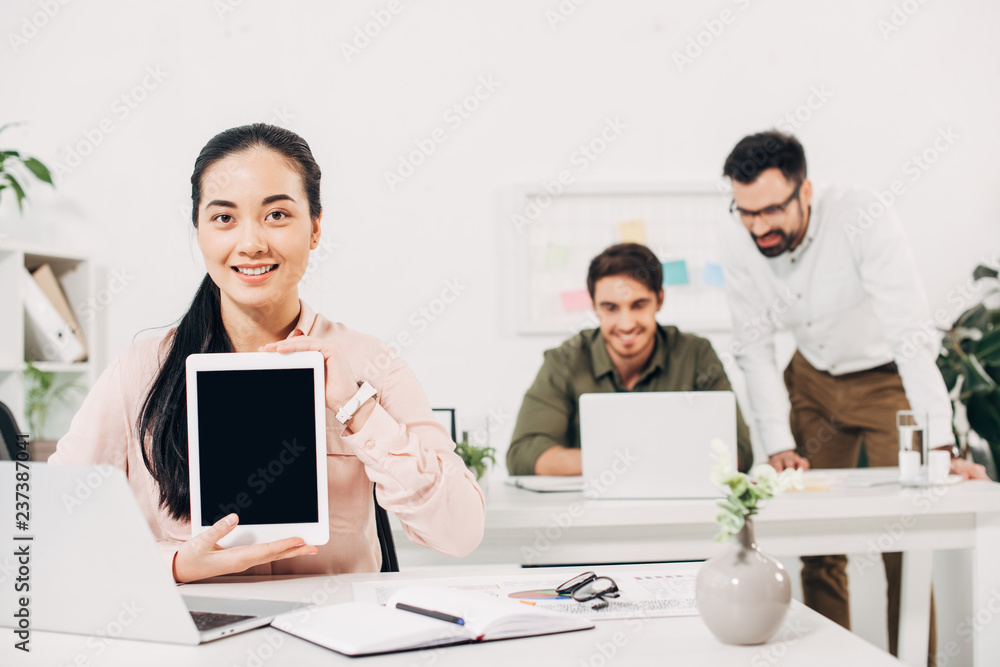 Female manager holding digital tablet with blank screen with male coworkers on background Female manager holding digital tablet with blank screen with male coworkers on background
