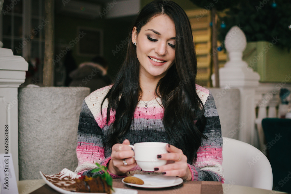 Portrait of young happy woman sitting in cafe and drinking tea with cookies