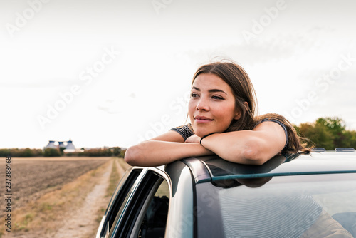 Smiling young woman looking out of sunroof of a car