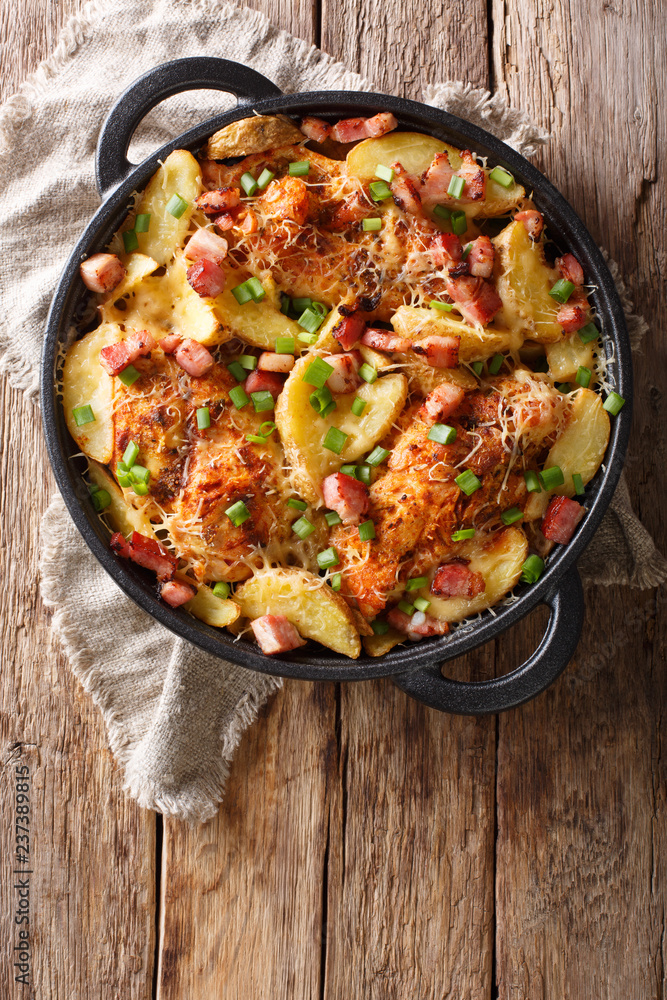 spicy chicken breast with potatoes, bacon and cheese close-up in a frying pan. Vertical top view