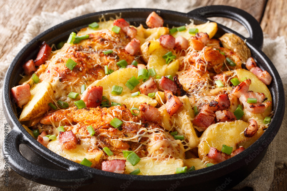 Delicious homemade baked chicken fillet with potatoes, bacon and cheese close-up in a frying pan. horizontal