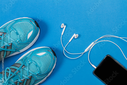 Zapatillas de deporte sobre fondo azul con teléfono móvil y auriculares. Vista superior. Copy space photo