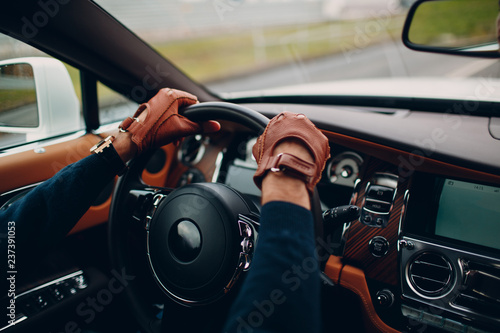 The hands of the driver in leather gloves, driving a moving car.