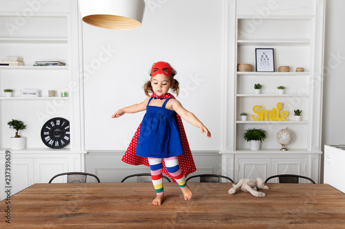 Little girl dressed up as superhero standing on kitchen table