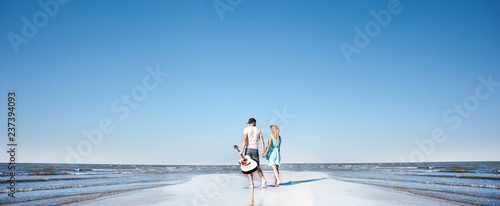 young couple in love with a guitar on the seashore.